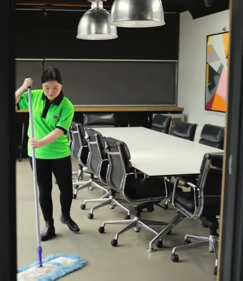 Cleaner dust mopping a conference room floor alongside the table and chairs
